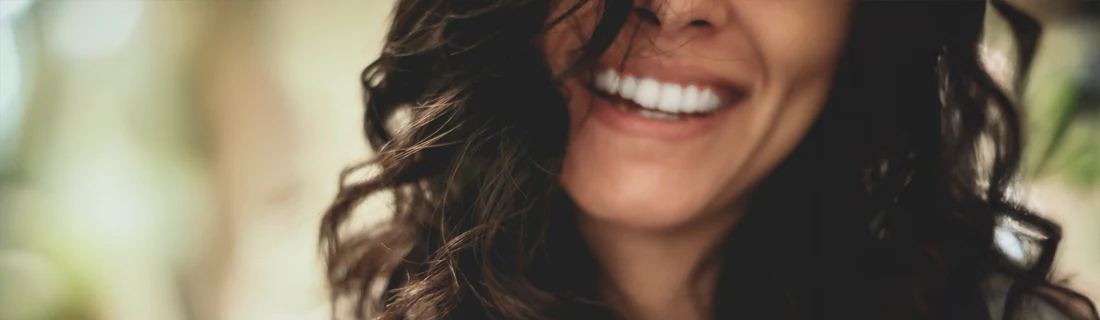 A close up of a woman smiling. She has dark curly hair.