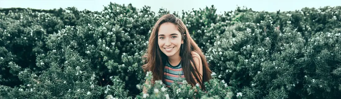 A woman smiling, while sitting in a rosemary bush.